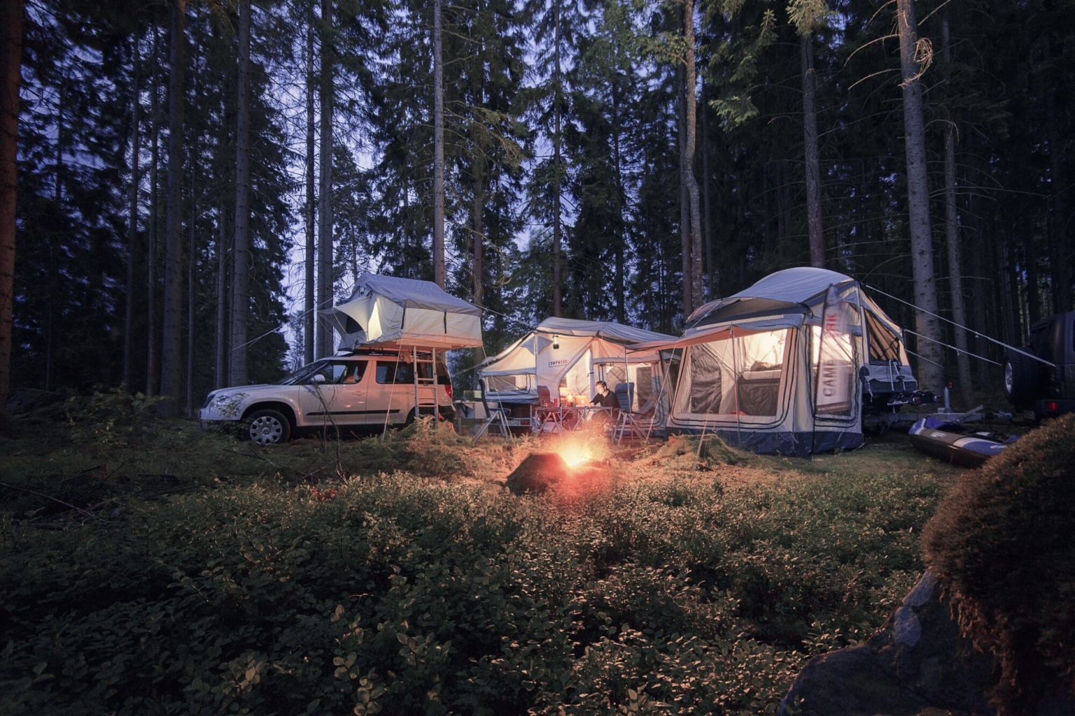 Camping mit Dachzelt im Wald. Auto mit Roof Tent, Vorzelt und Lagerfeuer bei Outdoor-Abenteuer und Roadtrip in der Natur