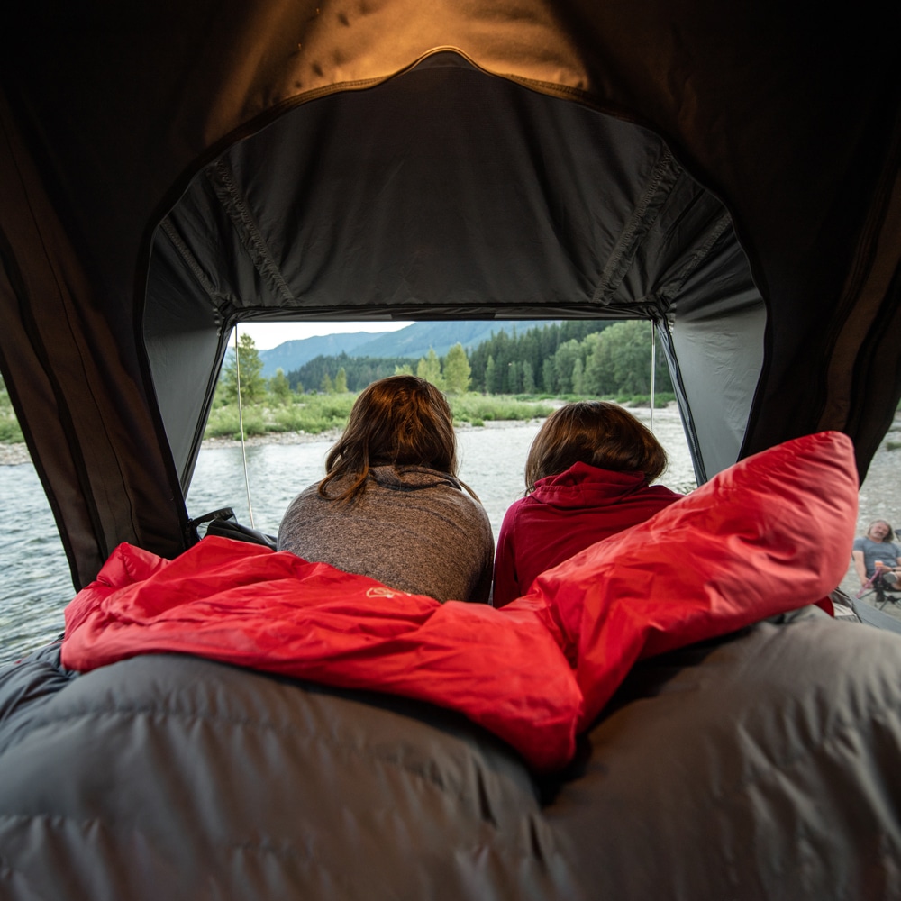 Two friends enjoy the view from their roof tent on the Audi A3