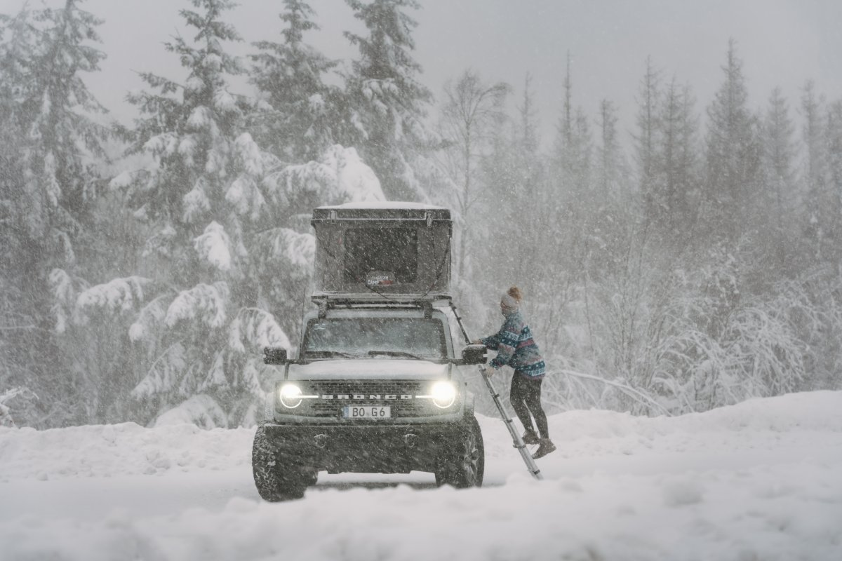 Frau steigt über die Leiter bei Schneesturm in ihr Hartschalen Dachzelt vom CAMPWERK