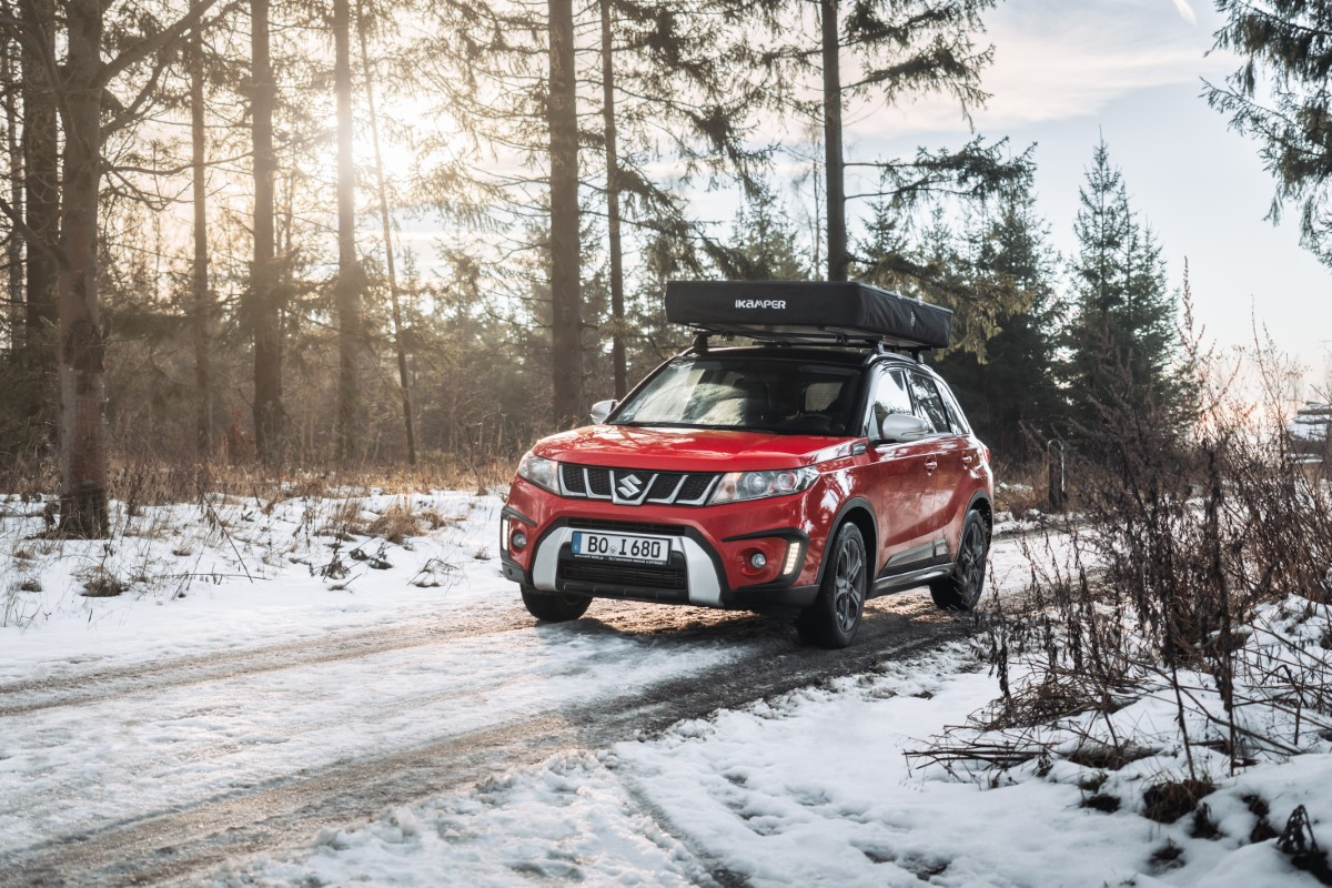 Roof tent on a red Suzuki driving through the forest in winter