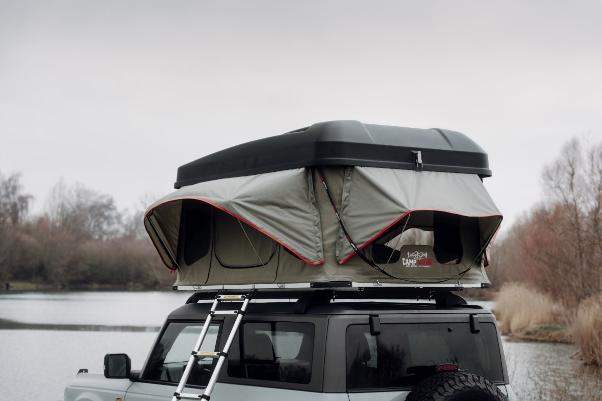 Nahaufnahme eines CAMPWERK-Dachzelts auf einem grauen Auto, das an einem See parkt