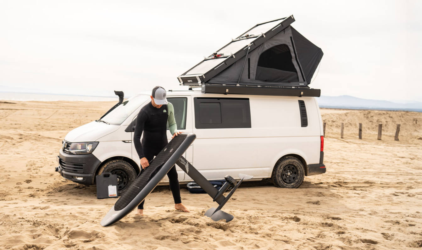 Surfer am Strand packt sein Equipment ein vor seinem Van mit BDV Hartschalen Dachzelt