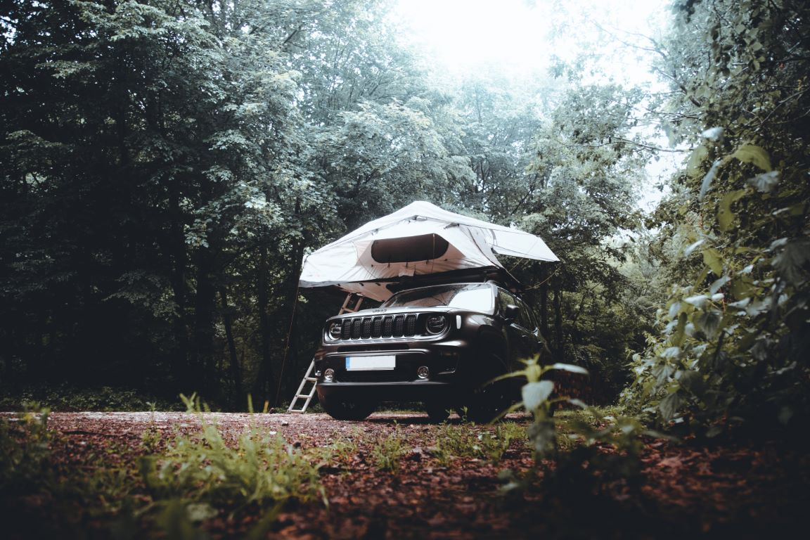 Un'auto nera con una tenda da tetto bianca CAMPWERK parcheggiata in un bosco.