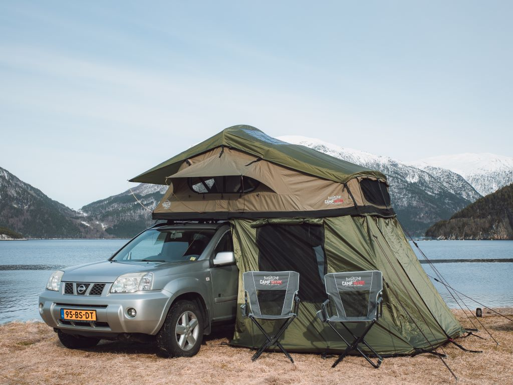 Tenda da tetto CAMPWERK verde su un'auto con sedie da campeggio e tettoia su un lago di montagna