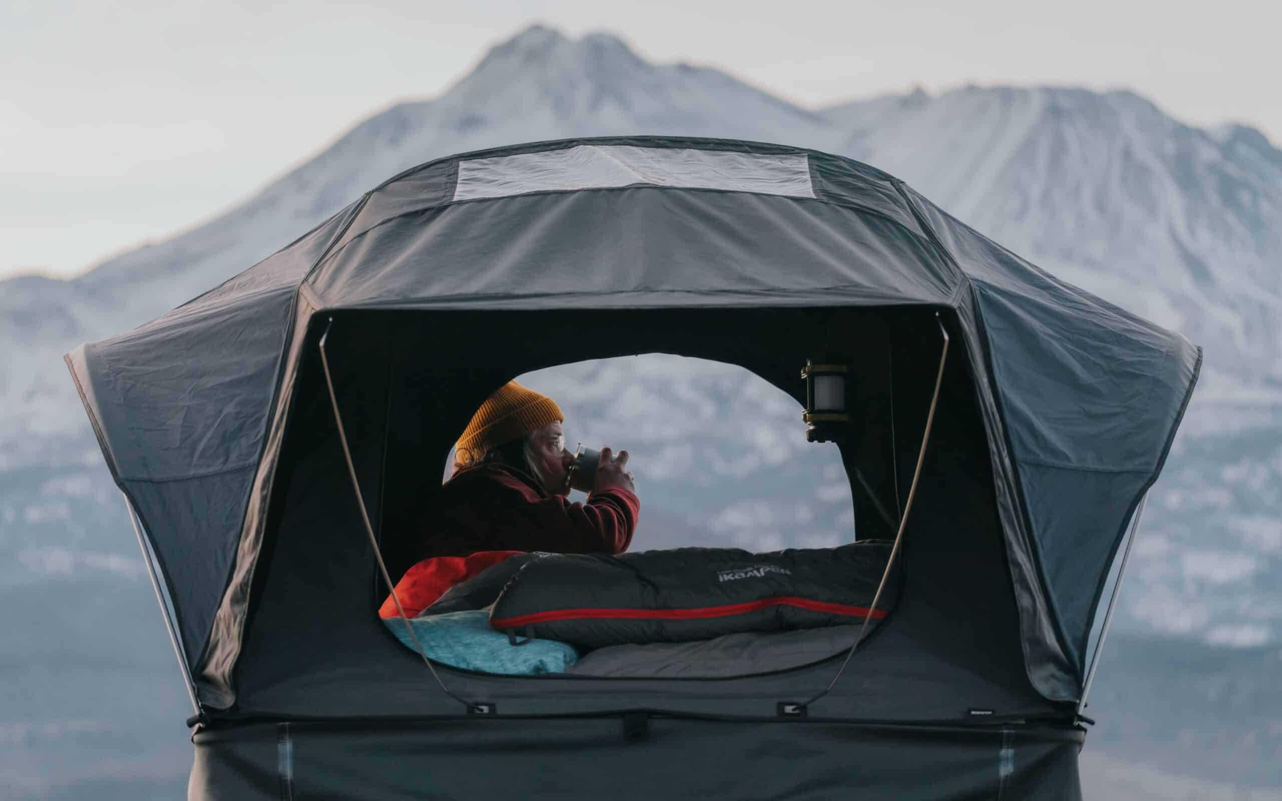 Woman drinking tea in her roof tent in the mountains