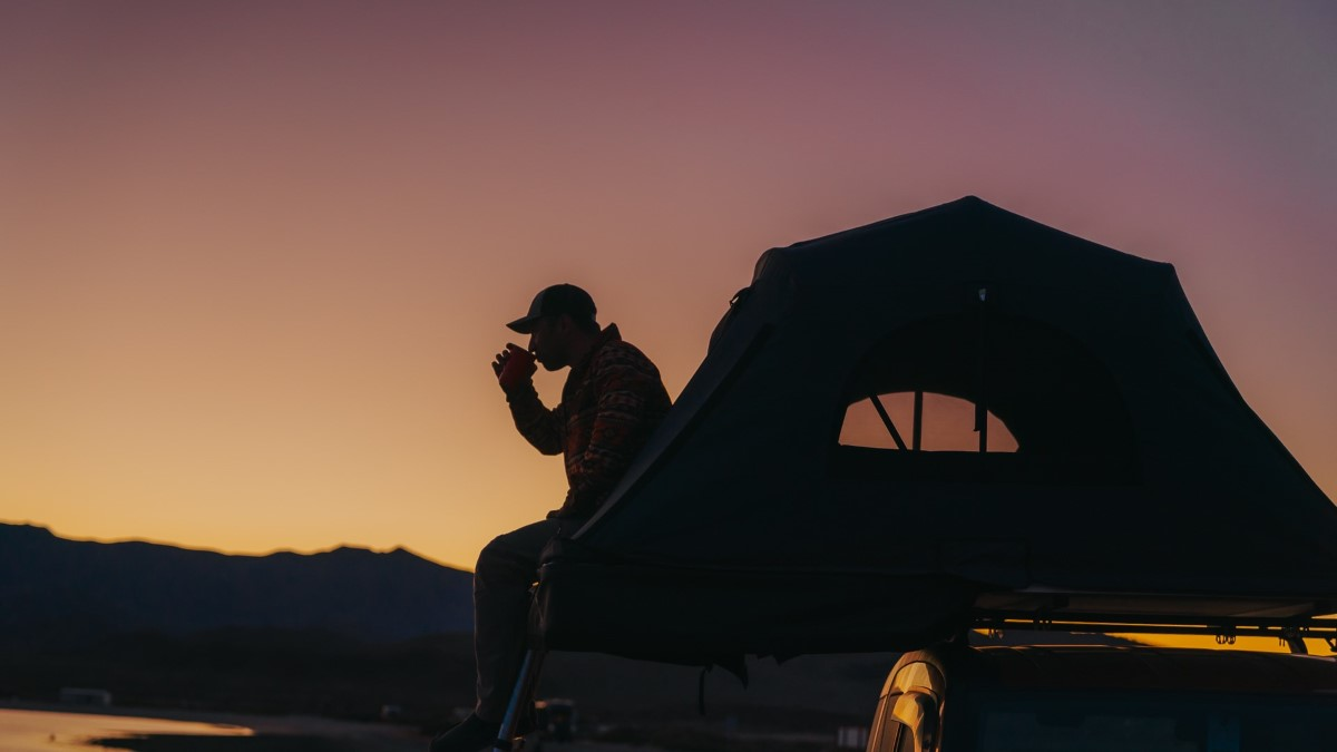 Man drinking tea in his roof tent on an Audi A4 at sunset