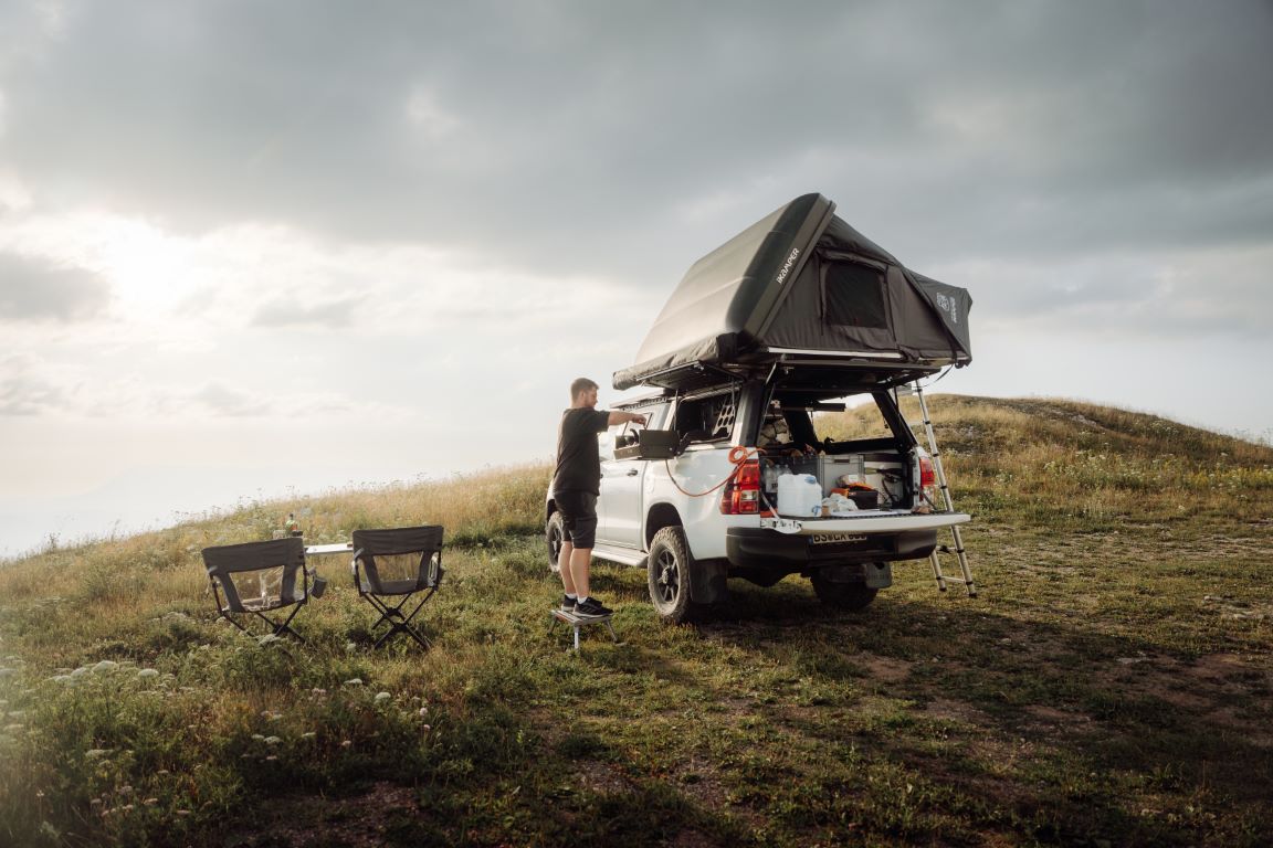 A person installs a roof tent alone on an off-road vehicle parked in a meadow in nature