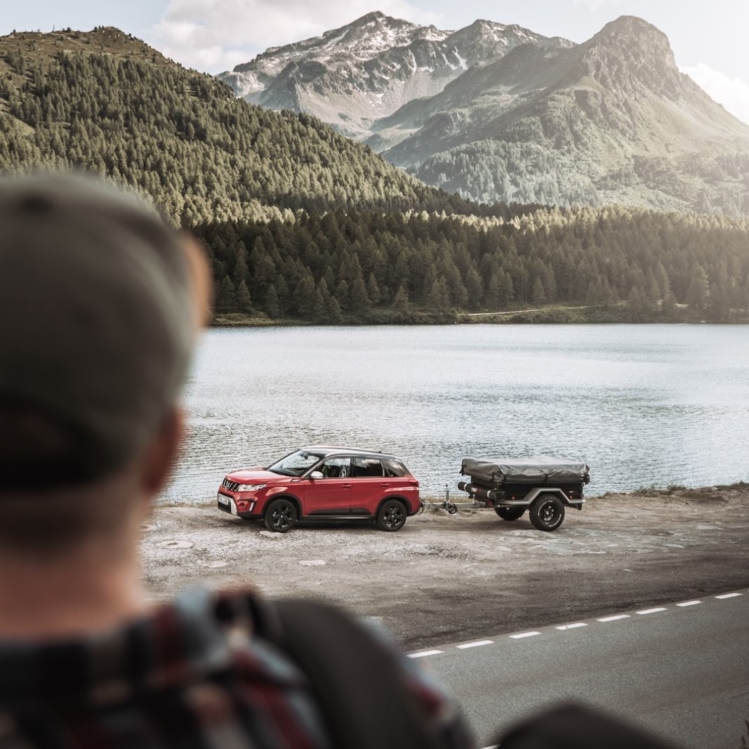 Person looking at a car with a tent trailer uncoupled by the lake