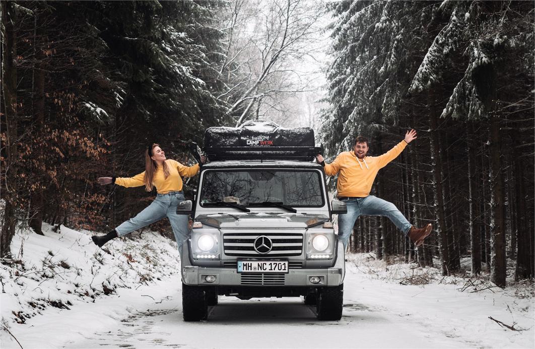 Couple next to their car with a roof tent on a snowy road