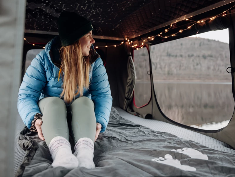 Camper sitting on a heating blanket in her roof tent in winter