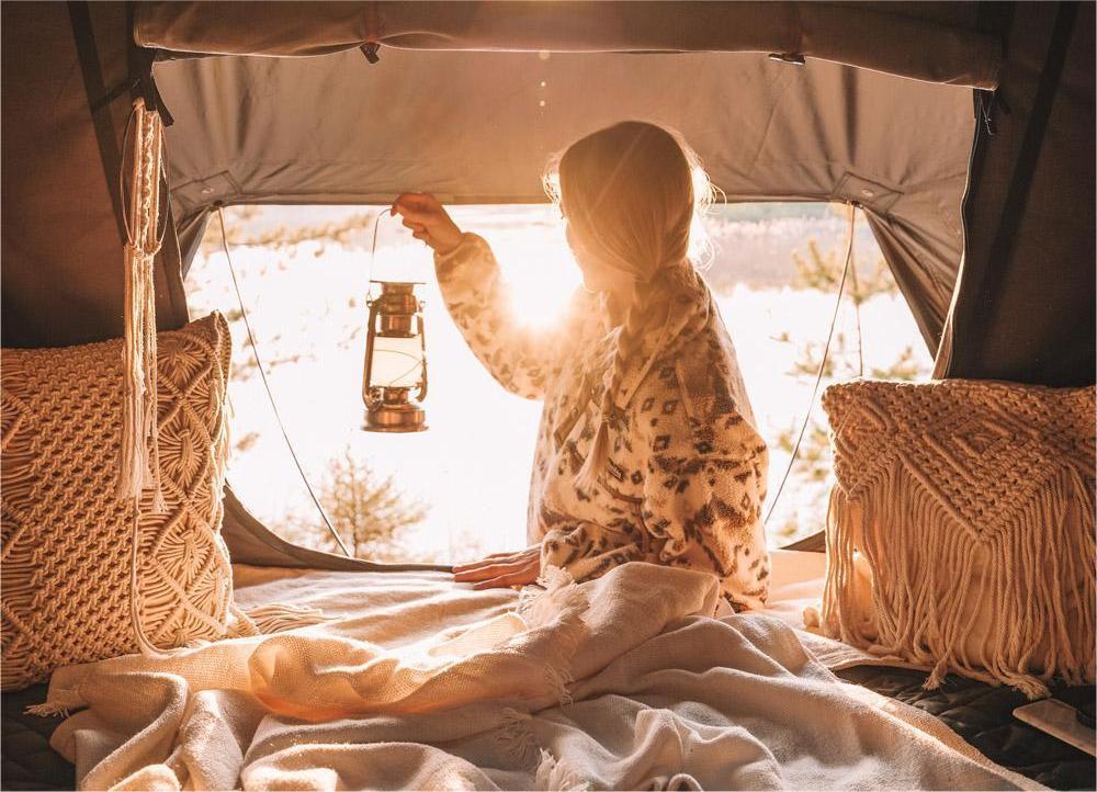 Woman looks out of the opening of her roof tent at dusk